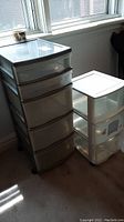 Two plastic storage drawer units on wheels, one with five drawers and one with three drawers, near a window on carpet.
