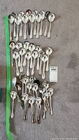 Top view showing 40 Queens plate soup spoons laid out on carpet with green measuring tape beside them.