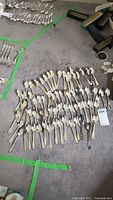 Overview of 72 silverware spoons laid out on a carpet, showing various sizes and patterns. Spoons appear tarnished and need cleaning.