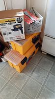 Stacked yellow Mastercraft toolboxes with black latches in photo beside Wagner power sprayer box and some loose hand tools in plastic crates.