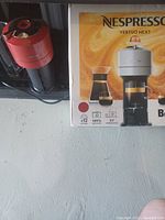 Red Nespresso Vertuo Next coffee maker next to original box showing product image and branding.