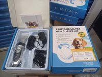 Opened box showing the professional cordless pet hair clipper, charger, multiple comb attachments, cleaning brush, lubricating oil and instruction manual inside the original packaging.