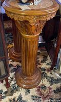Full view of carved pedestal plant stand on floral carpet, showing overall shape and size.