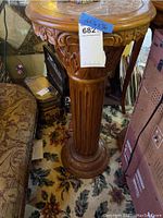 Full view of carved wood pedestal plant stand showing round top and base, vertical fluted column, and carved floral and leaf motifs.