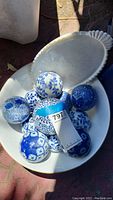 Top view of multiple blue and white patterned ceramic balls in a large white milk glass bowl with a matching platter underneath.