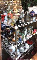 Wide view of multiple figurines, steins, and home decor items arranged on three wire shelves.