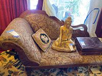 Full view of chaise lounge chair with pillow and other objects on seat, showing upholstery pattern and carved wooden arms