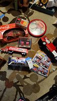 Photo showing multiple Coca-Cola collectible vehicles including die-cast trucks and a red and white wall clock with polar bear graphic.