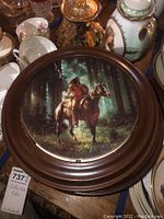 Photo of a round framed plate depicting a Native American figure on horseback in forest