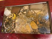 Top view of wooden display case showing various costume jewelry pieces inside including beaded necklaces, bracelets, and earrings.