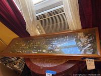 Full view of the large wooden display case with glass top housing various pieces of costume jewelry arranged inside on green felt