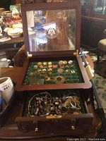 Collector case open with glass lid showing various costume jewelry pieces inside on felt.