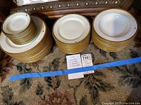 Three stacks of white porcelain plates with gold band trim and handwritten count card visible