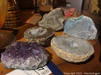 Photo showing five geodes, including amethyst and clear quartz varieties, showcasing natural outer surfaces and cut halves revealing crystalline interiors.