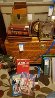 Photo showing Hammond clock, carved wooden chest, various wood boxes, a vintage brass frame clock, and three vintage books including Annie theatre memoir and others.