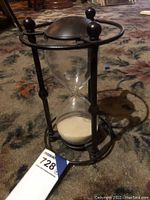 Side view of hourglass sand timer on carpet showing metal frame, glass body, and sand inside.