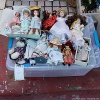 Top view of the plastic bin containing assorted Madame Alexander and heirloom dolls, some wearing vintage clothing and hats, along with a stuffed panda and rabbit toy.