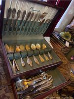 Opened wooden case showing organized silverplate flatware including knives, forks, spoons with green felt lining.