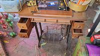 Front view of Singer sewing machine in wooden cabinet with open drawers showing storage compartments, metal treadle base visible underneath.