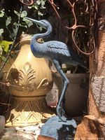 Side profile of the blue metal heron garden sculpture showing its long neck, beak, and feather details in an outdoor garden setting.