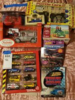 Photo showing the boxed Tonka Great Adventure Vehicles 9-pack, True Value 1913 Model T silver vehicle set, and boxed puzzle cars on a bed.