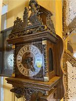 Front angled view of the clock showing detailed metal decorations and Roman numeral face.