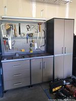 Overview of three cabinets and pegboard installed against wall, tools hanging on pegboard and items on countertop
