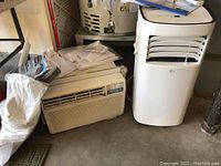 Two air conditioners side by side, portable unit on right and window unit on left