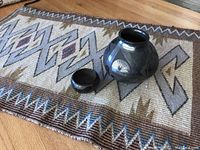Wide view of black on black pottery pieces on handwoven tapestry with geometric design