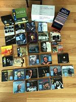 Top-down view of various classical and opera CD boxed sets and individual CDs arranged on floor, including Pavarotti albums and other classical composers/performers.