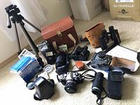 Wide overview of lot showing tripod, cameras, lenses, binoculars and cases on floor