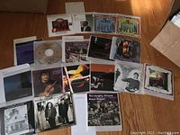 Photo shows a selection of CDs spread out on a floor with visible inserts, including various jazz, blues, folk album covers and artist photographs.