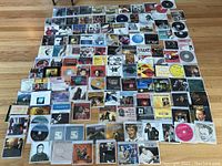 Overall layout of all CDs included in the lot laid flat on a floor, approximately 128 CDs total, showing a wide variety of artists and musical genres.