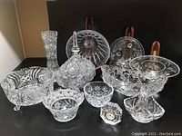 Photo showing group of various crystal serving bowls, vase, and Waterford clock arranged on black surface
