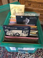 Top view of green plastic bin filled with paper sewing patterns, showing Folkwear 114 pattern and Edwardian Bridal Gown pattern visible.