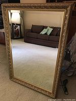 Full view of large rectangular framed mirror leaning against wall, showing reflection of room and couch.