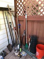 Full view showing variety of long handled garden tools, pruning shears, roll of wire mesh fencing and 5-gallon orange bucket