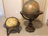 Two globes on wooden stands, larger one labeled Brandt with visible marks and scratches on wood.