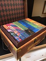 Photo showing the seven colorful hardback books neatly arranged in a card box trunk with 'Harry Potter' branding on front.