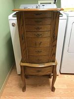 Front view of wooden jewelry armoire showing seven drawers with metal handles, side doors, and curved legs