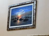 Framed serigraph art piece showing boats at sunset, hung on wall, capturing overall composition and colors.