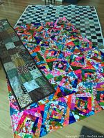 Set of two large quilts and one patchwork table runner displayed on the floor.