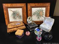 Overall lot showing vintage music boxes, wood prints, paperweights, and box of glass angels all on black surface.
