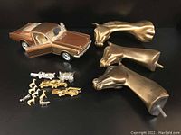 Photo showing the brown metallic Mustang model with open doors, the three large brass horse heads, and smaller metallic tie tacks arranged in front.