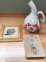 Grouped photo showing all three items: the Apache pottery water jug, the wood-framed sandpainting of a vase signed by Save, and the pottery wall hanging with figure in sandpainting style.