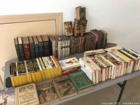 Overview of full lot on folding table showing paperbacks in front, cloth hardcovers in middle, leather-bound and assorted hardcovers at back