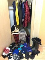 Closet corner with multiple jackets hanging, variety of hats displayed on shelves and floor, scarves and boots arranged below