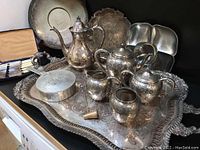 Image showing large ornate silver plated footed tray with detailed floral engraving, surrounded by the matching 4-piece tea service with sugar, creamer, teapot, and ginger jar bowl, along with other silver plated items and accessories.