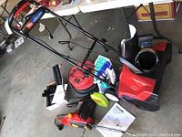 Full view of Toro 1800 Power Curve snowthrower and Homelite electric chainsaw with accessories including chain oil and manuals around them.