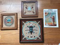 Three wooden framed Native American traditional sand paintings plus a softback book on Navajo Sandpainting Art. Paintings include various symbolic depictions with vibrant color.